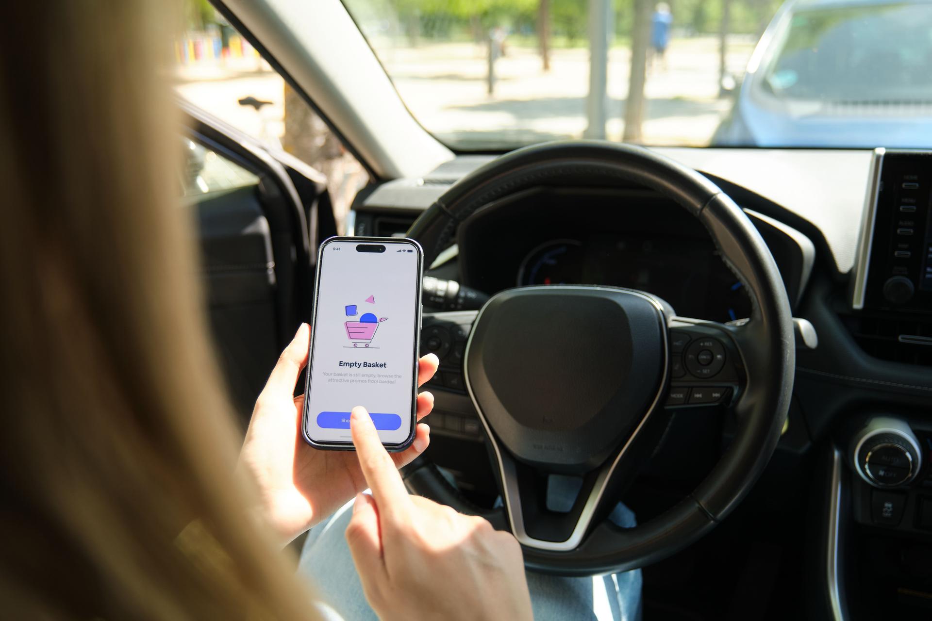 Woman using shopping app on smartphone in car with empty basket message